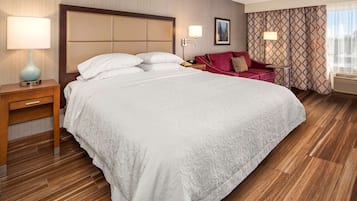Habitació d'hotel amb un llit gran, una nit de nit amb una làmpada, un sofà vermell i una cortina amb dibuixos.