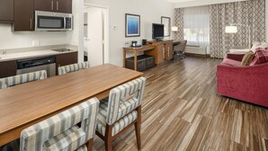 A modern hotel room with a wooden dining table, striped chairs, a red sofa, a flat-screen TV, a microwave, and a coffee maker. - Hampton Inn & Suites Seattle-North/Lynnwood (Lynnwood)