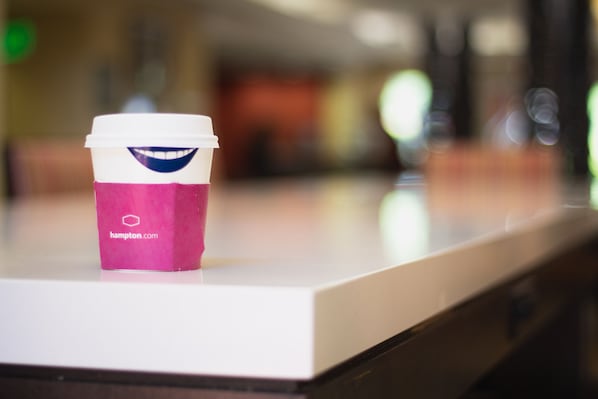 Una taza de café con tapa con forma de carita sonriente sobre una encimera.