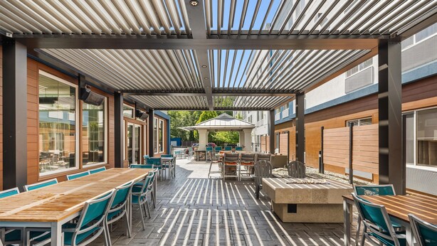 An outdoor dining area with wooden tables and chairs, a covered seating area, and a view of the building's exterior. - Hampton Inn & Suites Seattle-North/Lynnwood (Lynnwood)