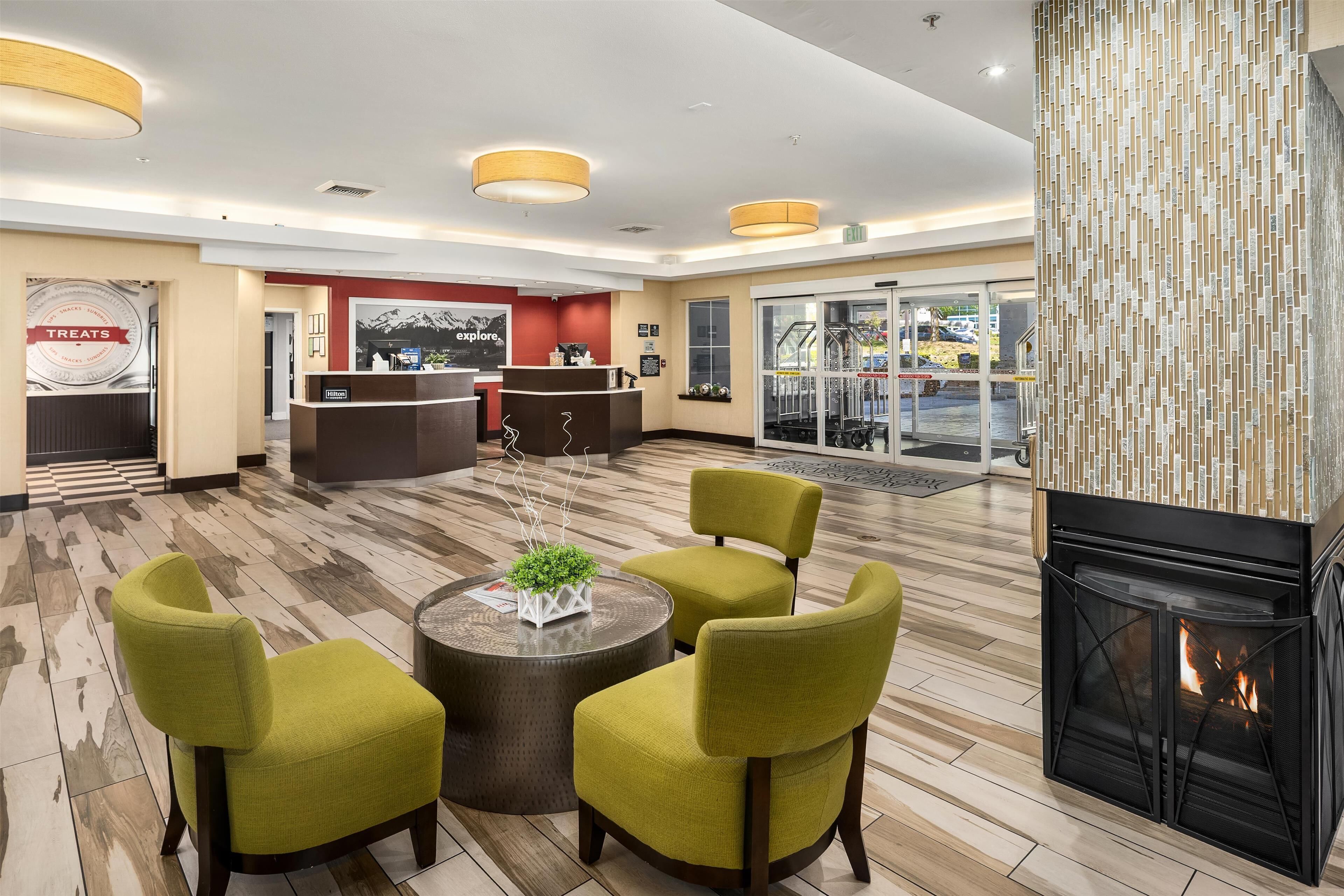 A lobby with a reception desk, a fireplace, and a seating area with green chairs and a round table.