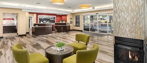A lobby with a reception desk, a fireplace, and a seating area with green chairs and a round table.