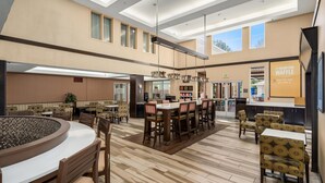 A spacious hotel lobby with multiple dining areas, a central bar, and a view of the outdoors. - Hampton Inn & Suites Seattle-North/Lynnwood (Lynnwood)