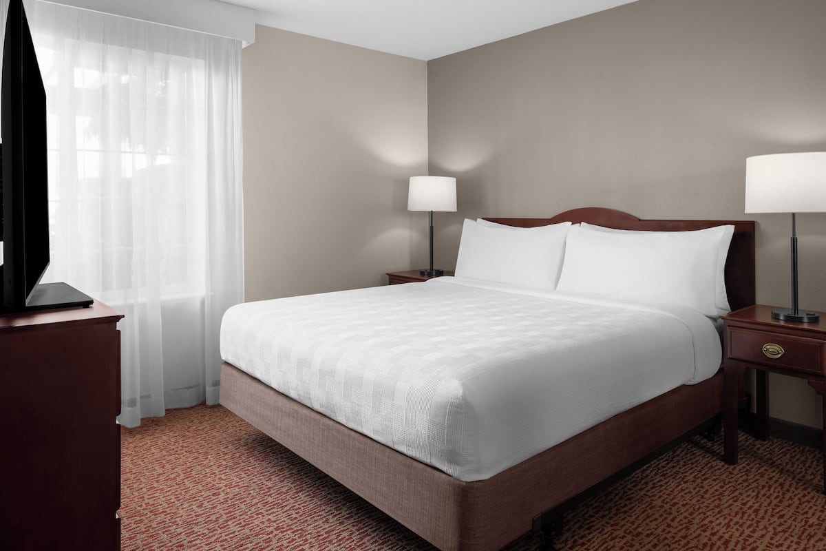 Een hotelkamer met een groot bed, twee nachtkastjes met lampen, een houten nachtkastje en een tapijtelig vloerkleed met een rood patroon.