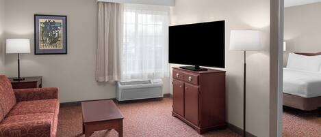 A hotel room with a bed, a TV, a desk, a chair, a lamp, and a picture on the wall.