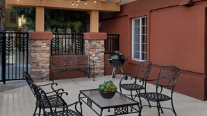 Un patio al aire libre con pared de piedra, pérgola de madera con luces colgantes, una parrilla y sillas y mesas de metal.