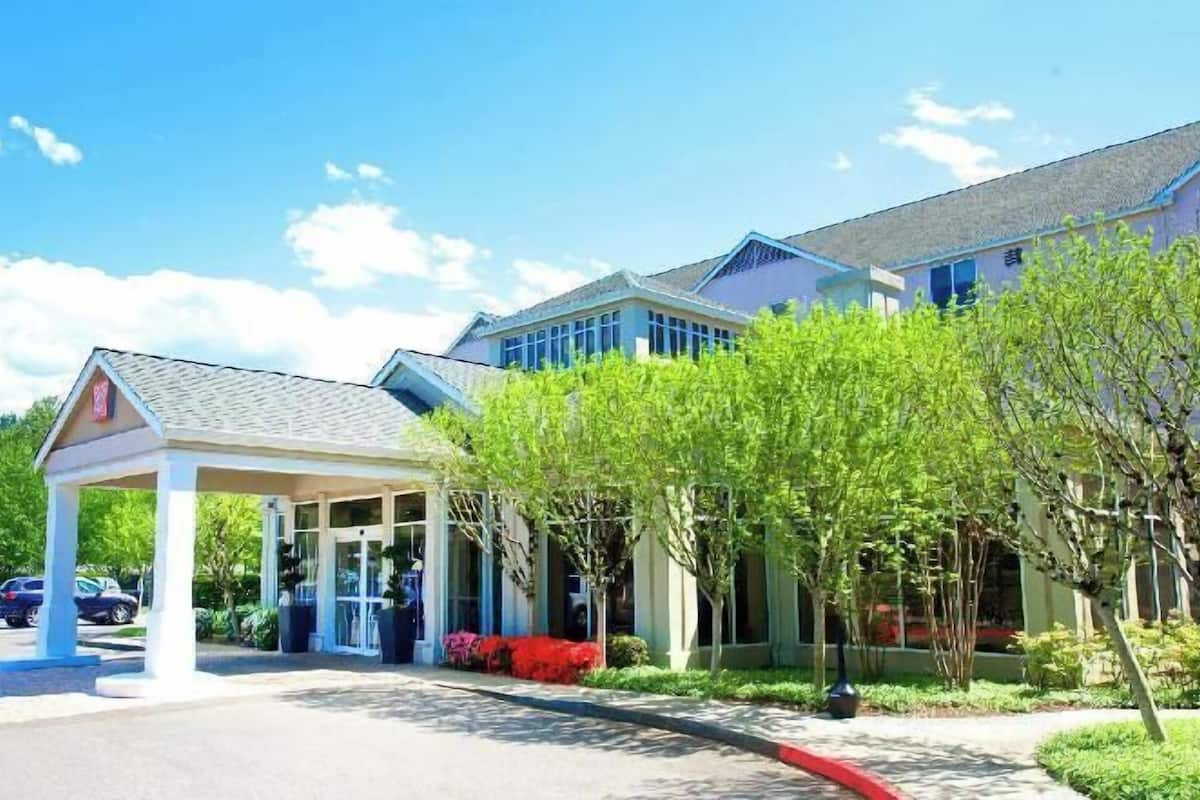 A hotel with a covered entrance, a parking lot, and a building with large windows.