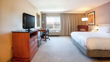 A hotel room with a bed, a desk with a television, a chair, and a window with curtains.