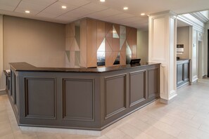 A reception area with a dark-toned reception desk, a geometric patterned wall, and a tiled floor. - Delta Hotels by Marriott Huntington Downtown (Huntington)