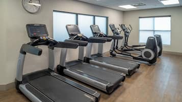 A gym with treadmills, ellipticals, and a digital clock on the wall.