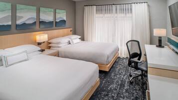 A hotel room with two beds, a desk, a chair, and artwork on the wall.