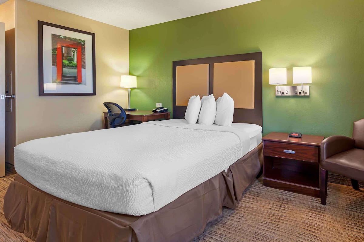 Une chambre d’hôtel avec un grand lit, un bureau avec une chaise, une lampe et un tableau au mur.
