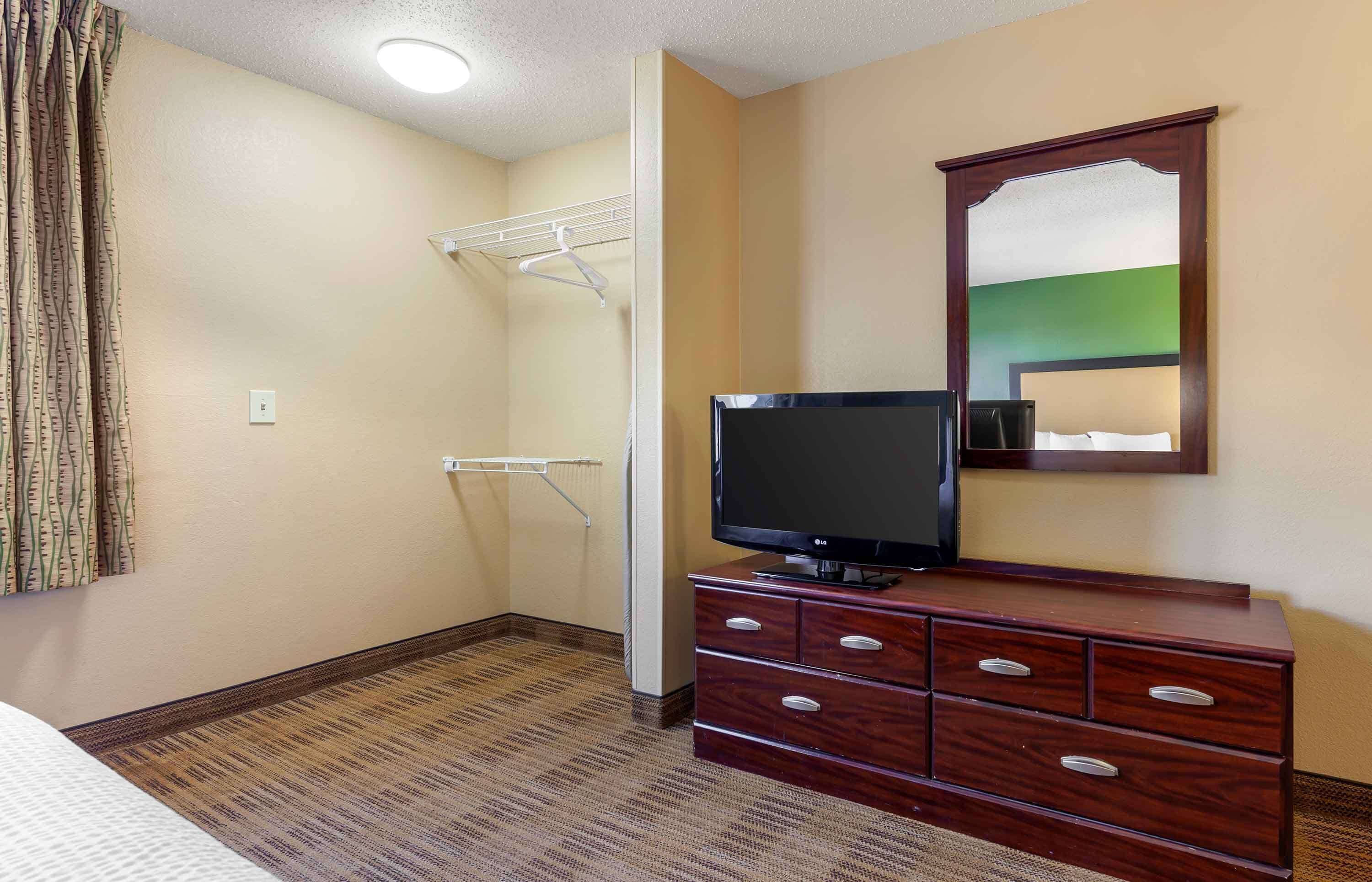 A hotel room with a TV on a dresser, a mirror, a coat rack, and a shower area.