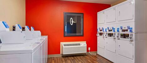 Une buanderie équipée de plusieurs machines à laver et de plusieurs sèche-linge, avec un mur rouge et un tableau encadré.