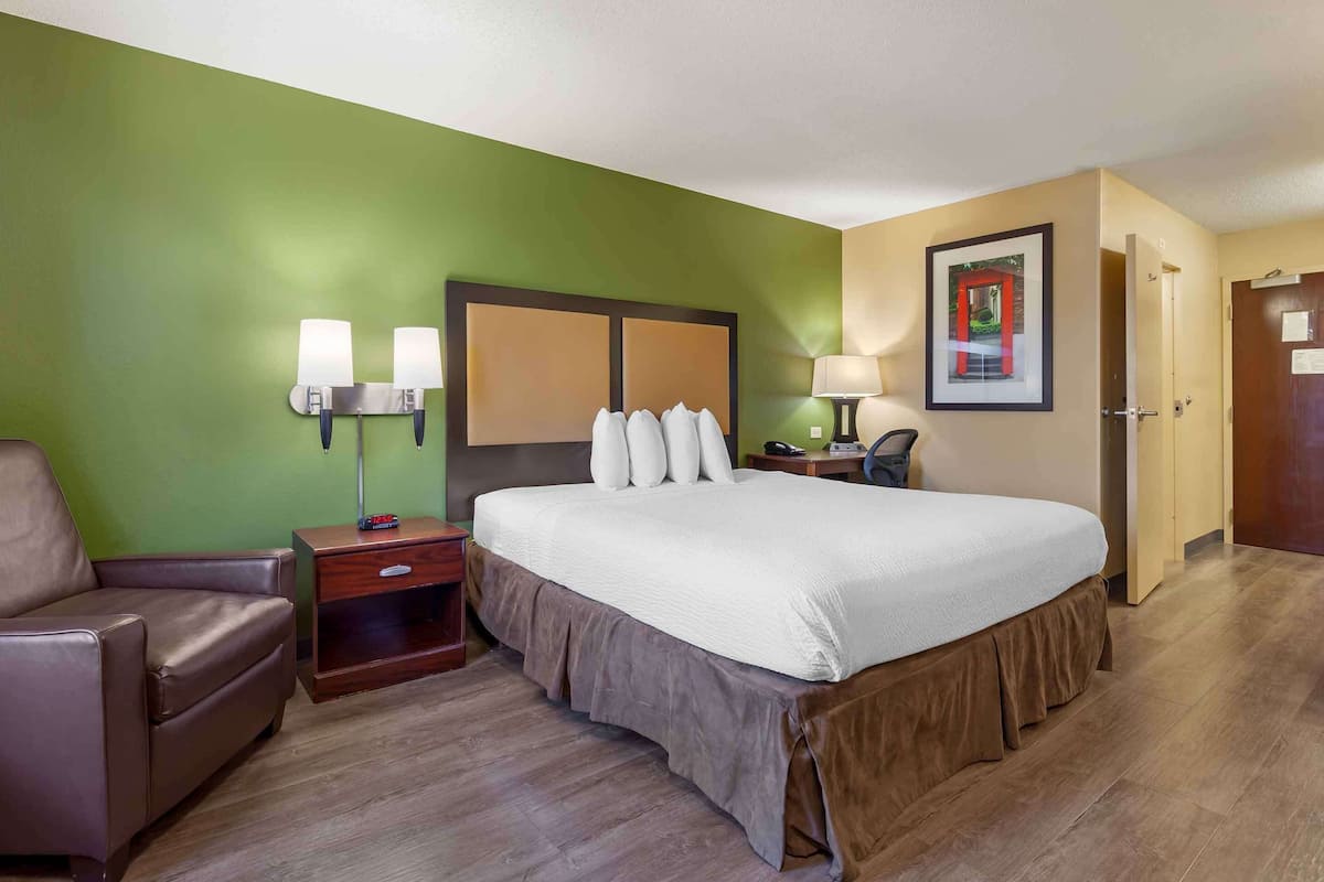 Une chambre d’hôtel avec un grand lit, une table de chevet avec une lampe, une chaise et un tableau encadré au mur.