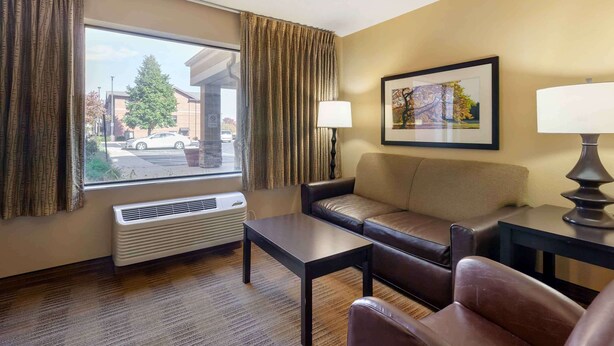 Une chambre d’hôtel avec un canapé en cuir, une petite table, un lampadaire, un tableau encadré au mur et une fenêtre avec des rideaux.