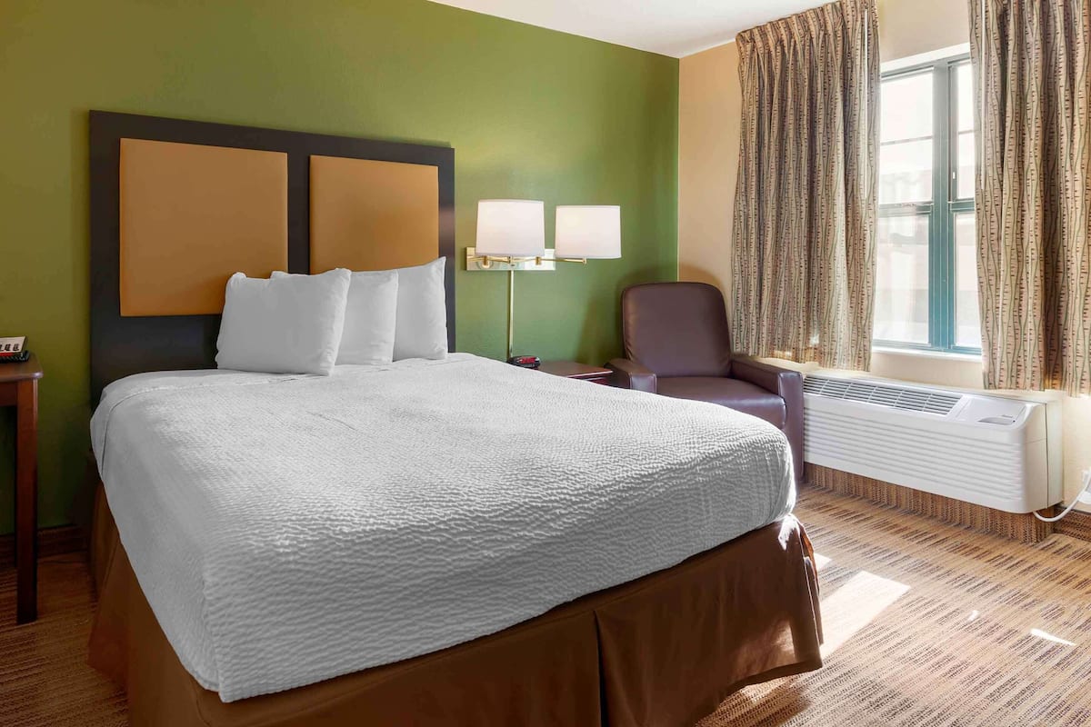 Une chambre d’hôtel avec un grand lit, un bureau avec une lampe, une chaise et une fenêtre avec des rideaux.