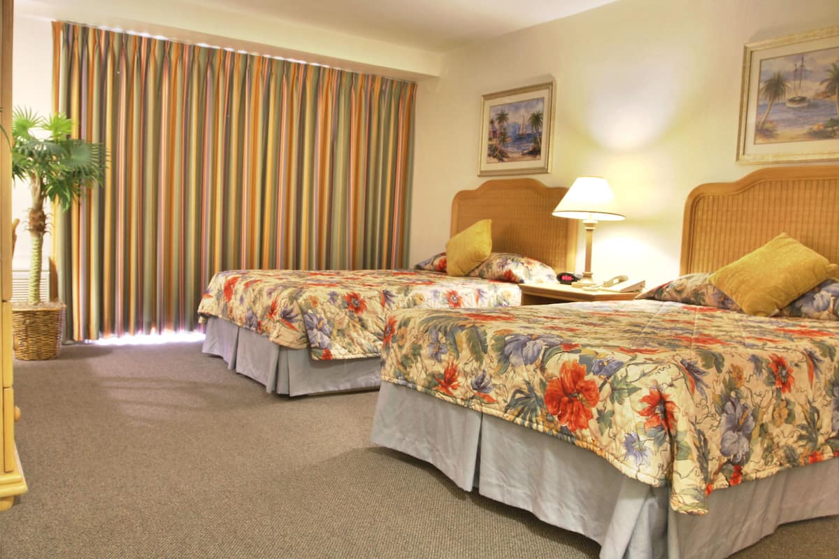 Quarto de hotel com duas camas, uma janela grande com cortinas, uma luminária e um quadro na parede.