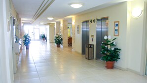 A hotel corridor with tiled floors, potted plants, and two elevators.