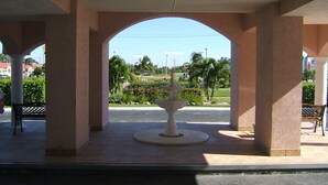 An outdoor covered area with a central fountain, surrounded by columns and benches.
