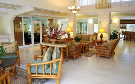 A spacious lobby with a high ceiling, a central seating area with wicker furniture, and a large decorative plant.