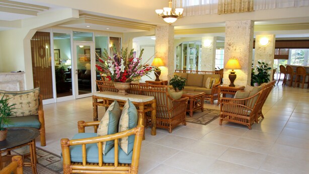 A spacious lobby with a high ceiling, a central seating area with wicker furniture, and a large decorative plant.