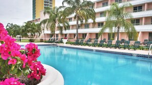 A swimming pool with lounge chairs and palm trees, surrounded by a hotel building.