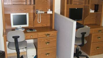 A wooden office cubicle with a desktop computer, a telephone, and a desk lamp.