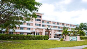 A pink multi-story hotel with a central courtyard, a signboard, and a well-maintained lawn.