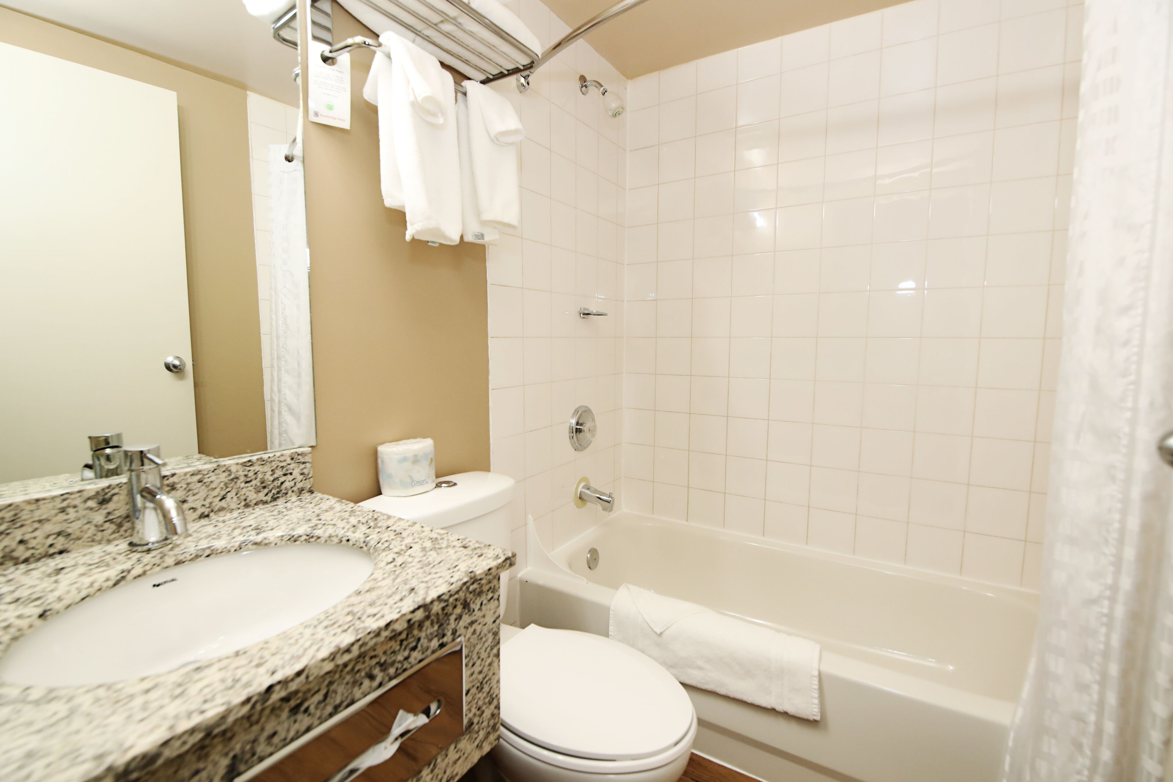 A bathroom with a granite countertop sink, a toilet, a bathtub, and a shower curtain.