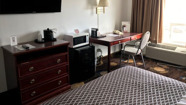 A hotel room with a bed, a desk with a computer, a TV, a lamp, a chair, a microwave, a coffee maker, and a telephone. - Stonebridge Hotel (Fort McMurray)