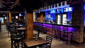 A bar area with multiple seating arrangements and a counter with a blue-lit backdrop. - Stonebridge Hotel (Fort McMurray)