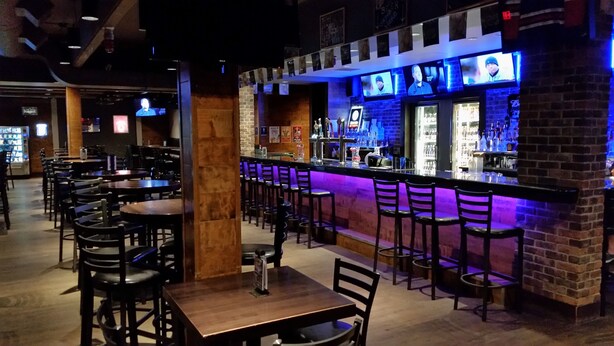 A bar area with multiple seating arrangements and a counter with a blue-lit backdrop. - Stonebridge Hotel (Fort McMurray)