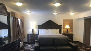 A hotel room with a large bed, a leather sofa, a dresser, and a mirror. - Stonebridge Hotel (Fort McMurray)