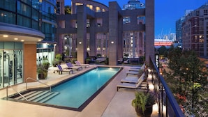 A rooftop pool area with lounge chairs, a swimming pool, and a view of a bridge.