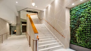 A modern staircase with marble steps and wooden handrails, leading to a lobby area with a green vertical garden wall.