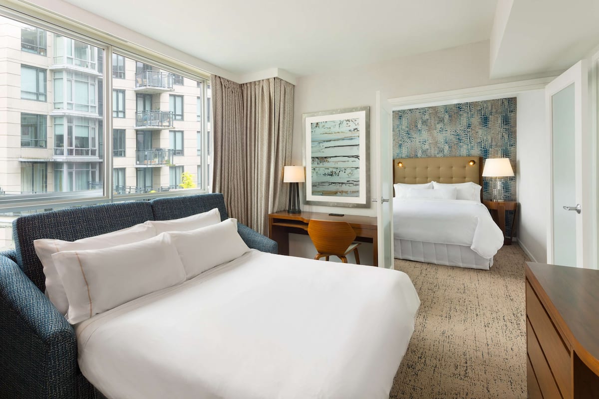 A hotel room with a large bed, a desk, a chair, and a view of the building outside.