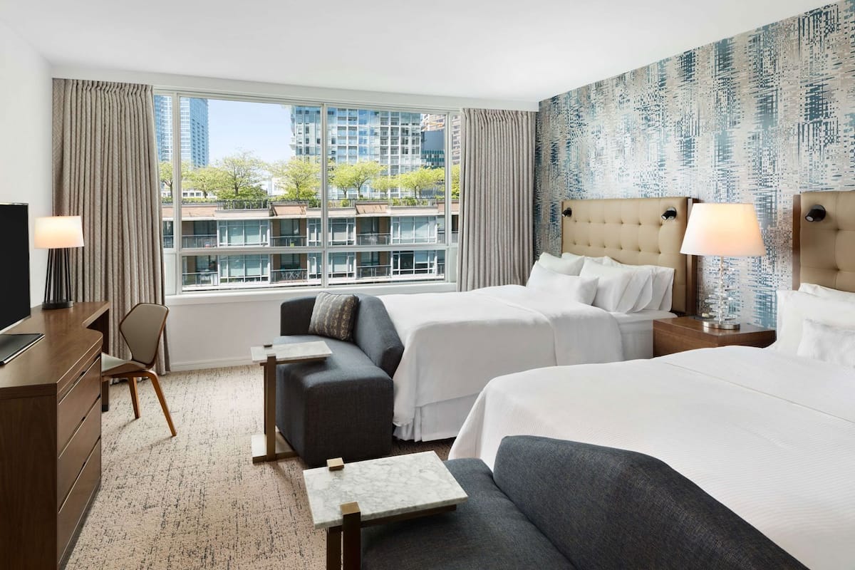 A hotel room with two beds, a sofa, a desk, and a TV.