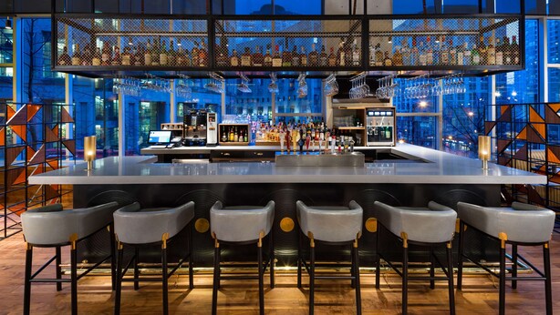 A bar with a high ceiling, multiple liquor bottles, and a bar counter with stools.
