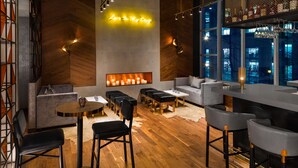 A modern bar area with wooden flooring, bar stools, and a neon sign reading "Love Is My Drug".