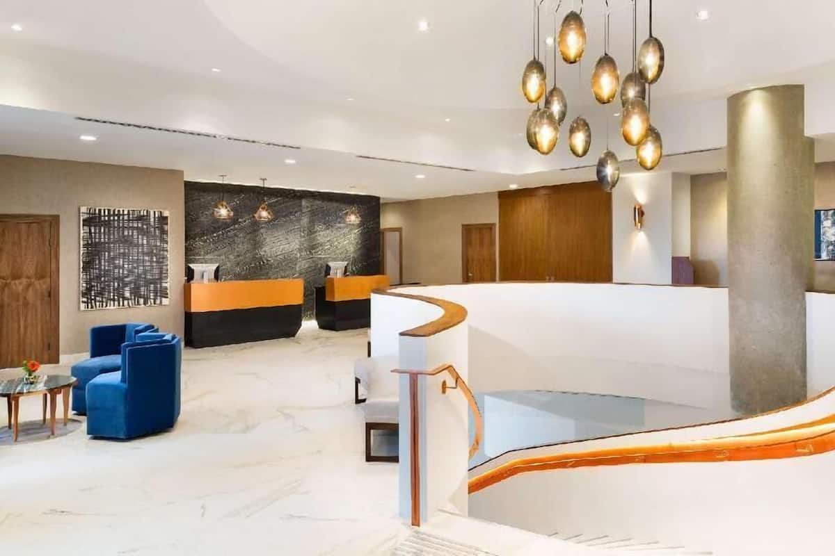 A modern hotel lobby with a reception desk, seating area, and a staircase.