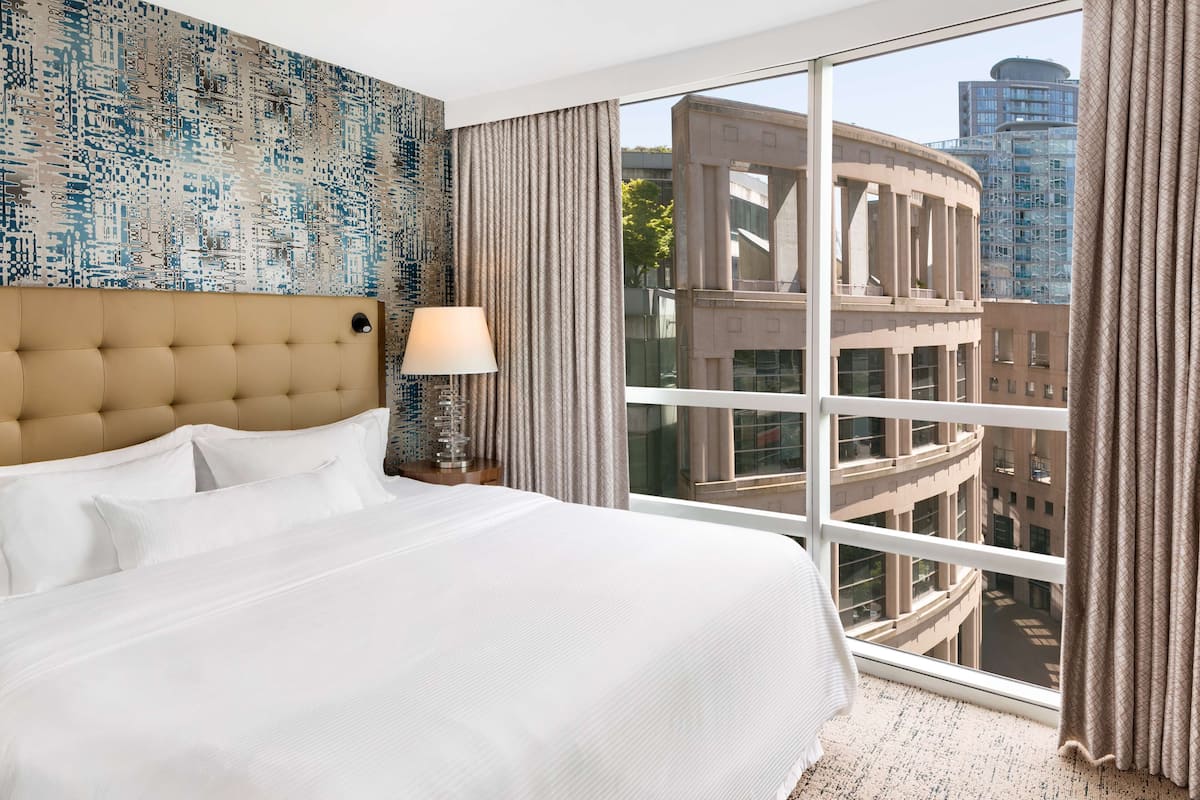 A hotel room with a large bed, a view of the city, and a patterned wall.