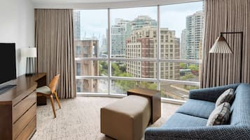 Ett modernt hotellrum med ett stort fönster, en soffa, ett skrivbord och en TV.