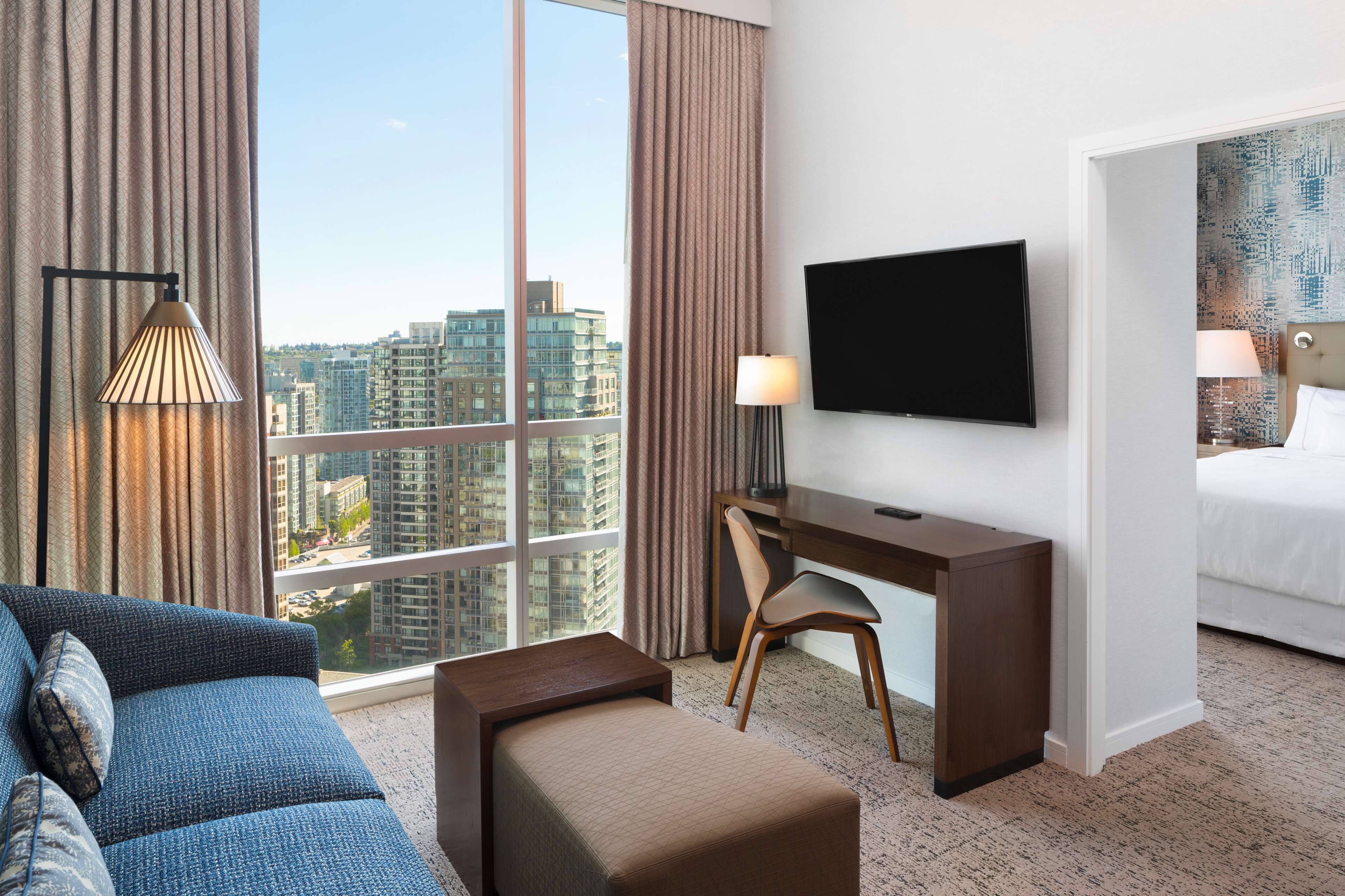 Une chambre d’hôtel dotée d’une grande fenêtre, d’un téléviseur à écran plat, d’un bureau, d’une chaise, d’un canapé et d’un lit.