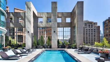Une piscine sur le toit, agrémentée de chaises longues, de plantes en pot et, en arrière-plan, un bâtiment moderne doté de grandes fenêtres.