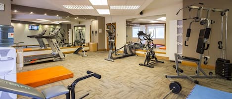 Un gimnasio con máquinas de cardio, equipo de levantamiento de pesas y un espejo grande.