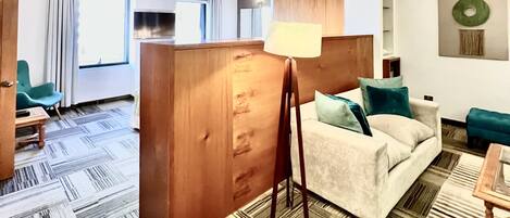 A hotel room with a sofa, a standing lamp, a TV, and a partition wall.