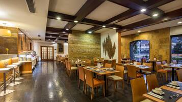 A restaurant with a modern interior, featuring wooden tables and chairs, a stone wall, and a view through a large window.