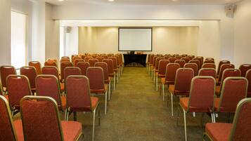 A conference room with rows of red chairs, a projector screen, and a table at the front.