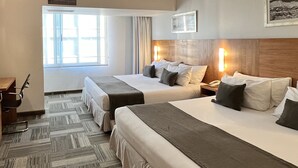 Habitación de hotel con dos camas, un escritorio y una silla. Hay una ventana con cortinas, un cuadro en la pared y un teléfono en la mesita de noche.